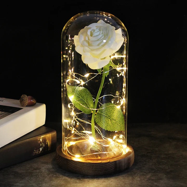 Artificial rose under a clear dome with LED string lights around the stem, on a round wooden base - white