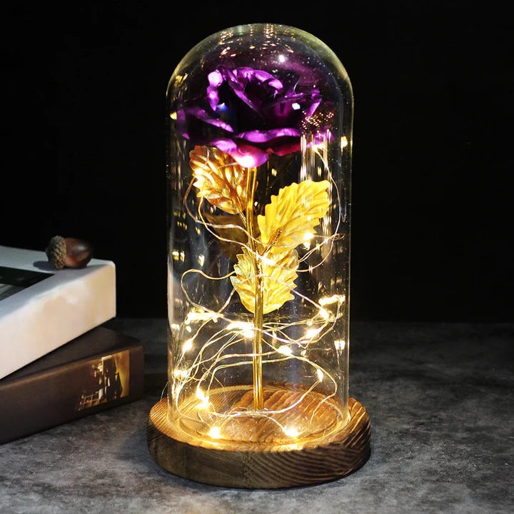 Artificial rose under a clear dome with LED string lights around the stem, on a round wooden base - purple