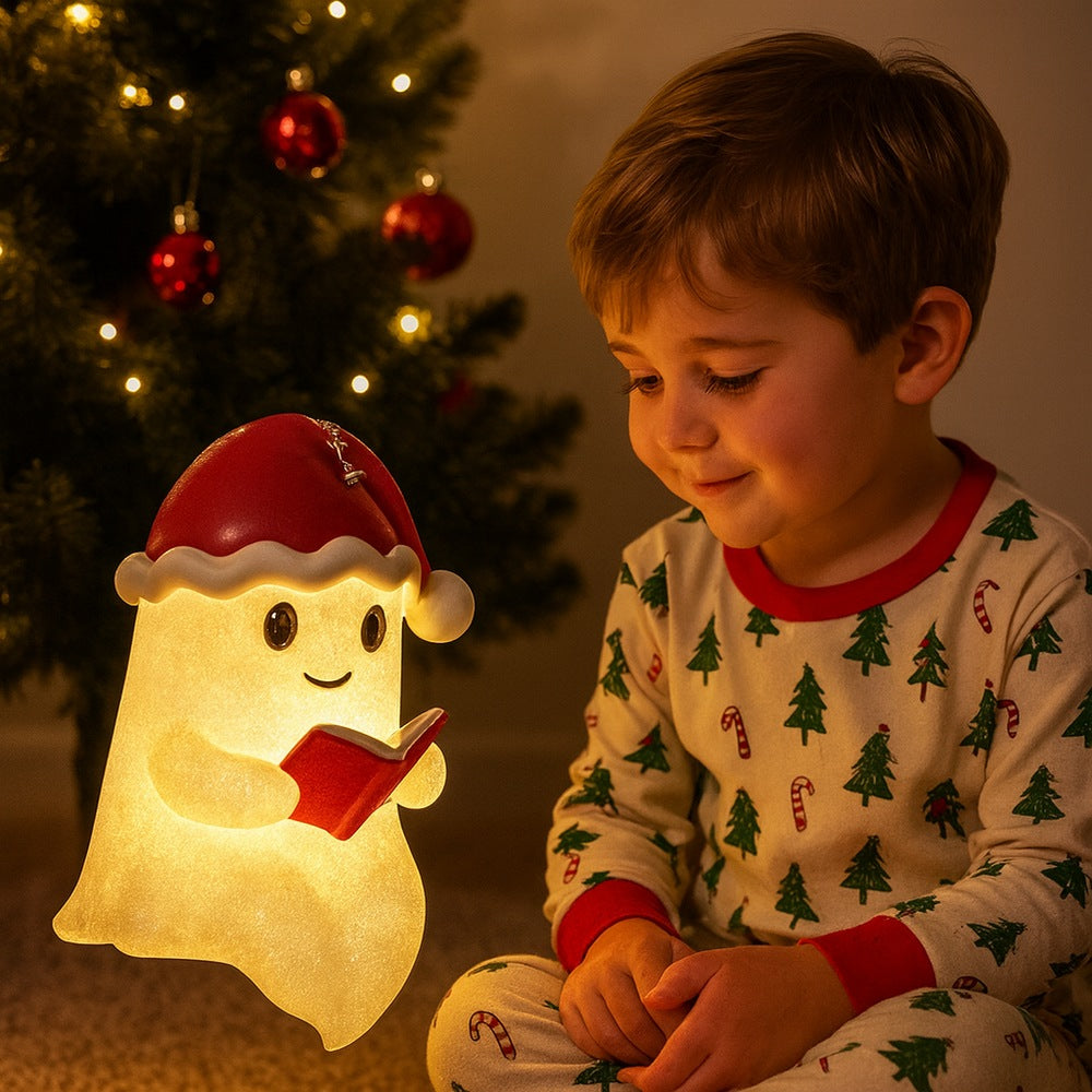 White ghost lamp in a red Santa hat with a bell, holding a red book and glowing warm yellow
