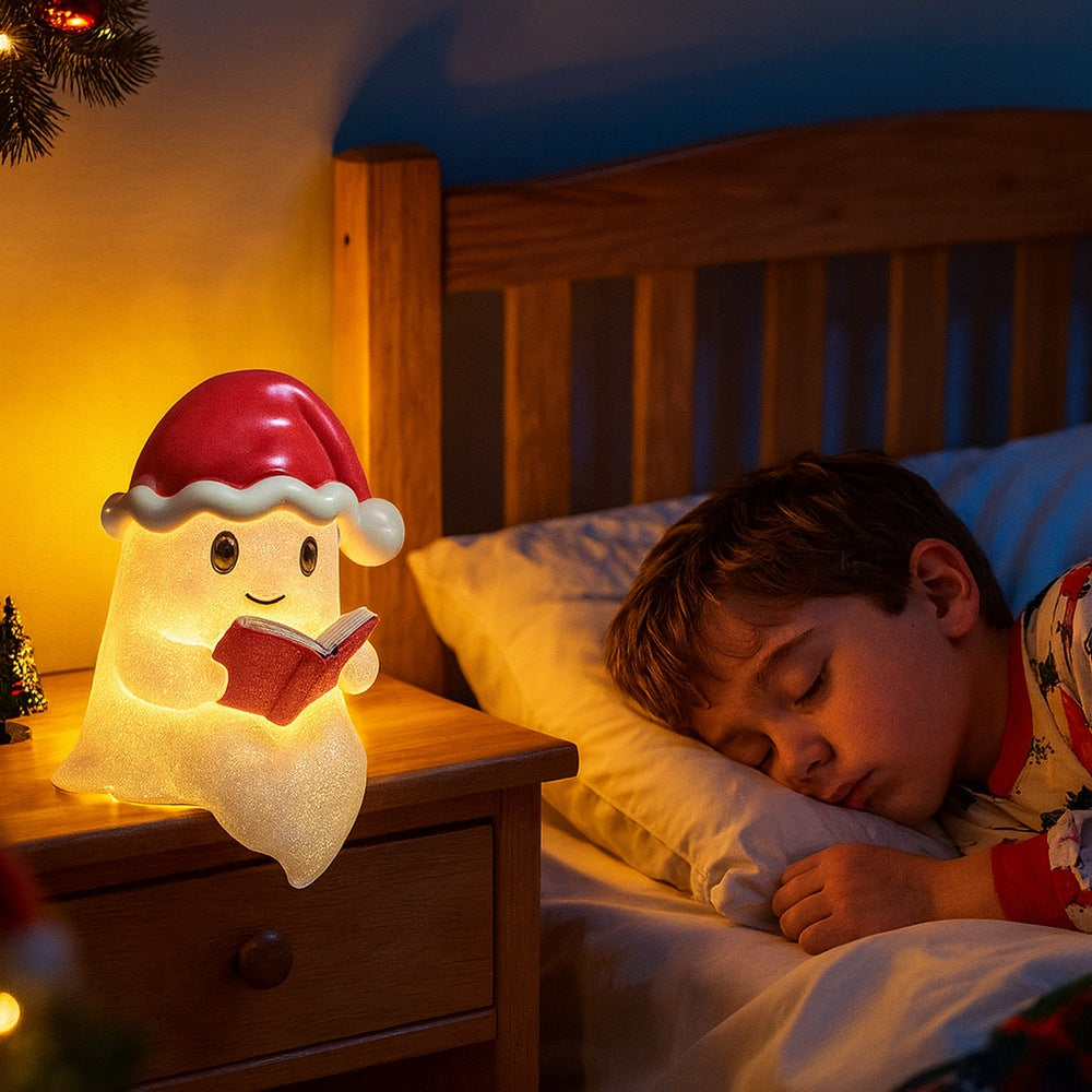 White ghost lamp in a red Santa hat with a bell, holding a red book and glowing warm yellow