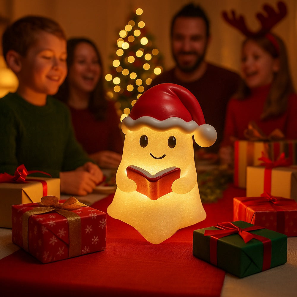 White ghost lamp in a red Santa hat with a bell, holding a red book and glowing warm yellow
