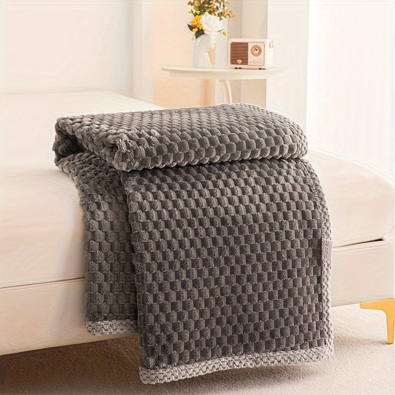 Fleece throw with a block texture and knitted trim draped over a bed - dark grey