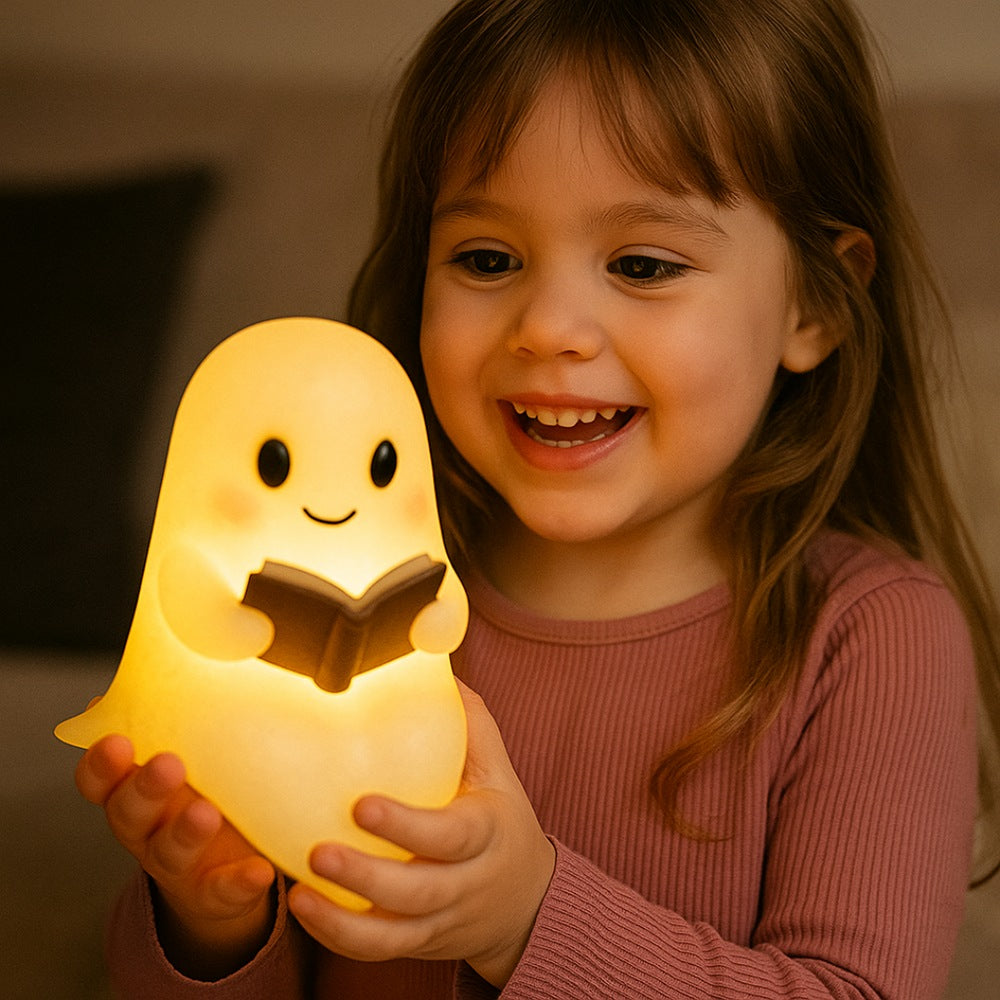 White ghost lamp with black eyes and pink cheeks holding an open brown book, glowing warm yellow
