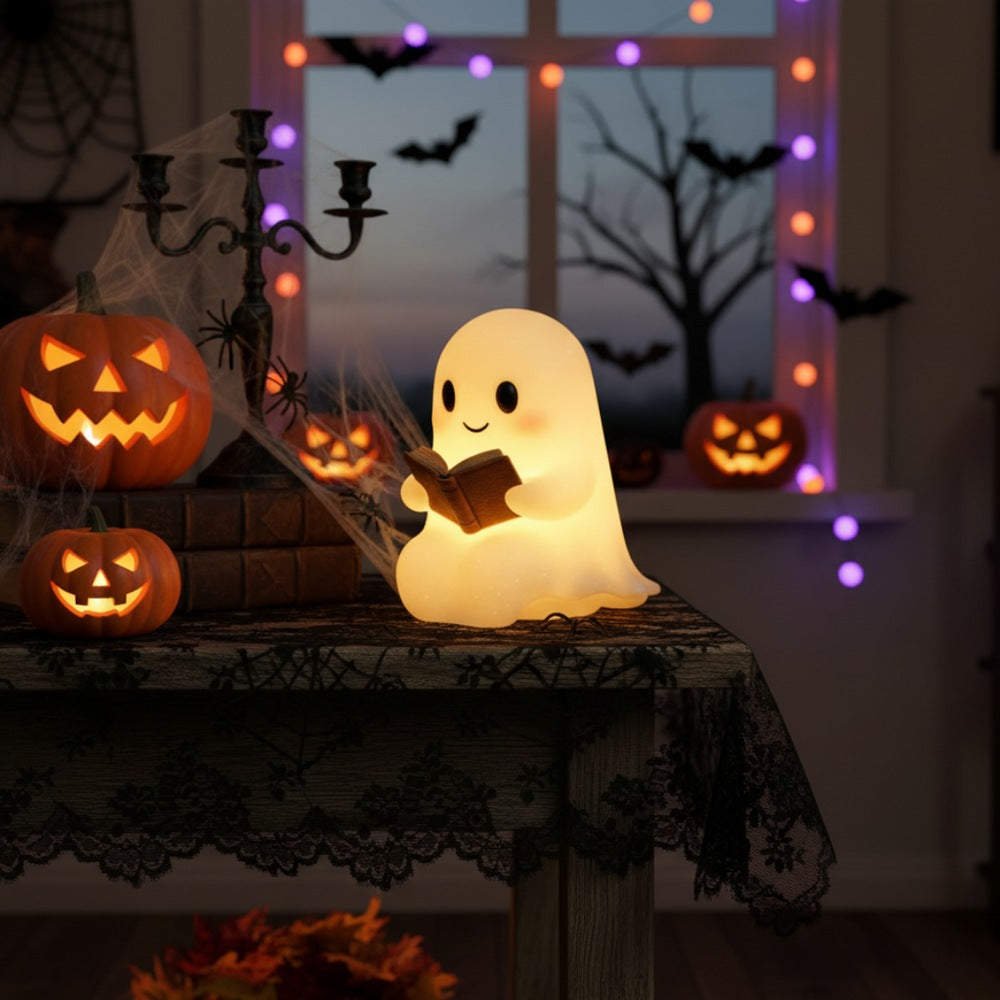 White ghost lamp with black eyes and pink cheeks holding an open brown book, glowing warm yellow