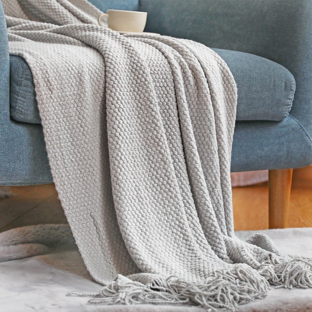 Knitted throw with a bobble texture and tassels over a sofa - light grey