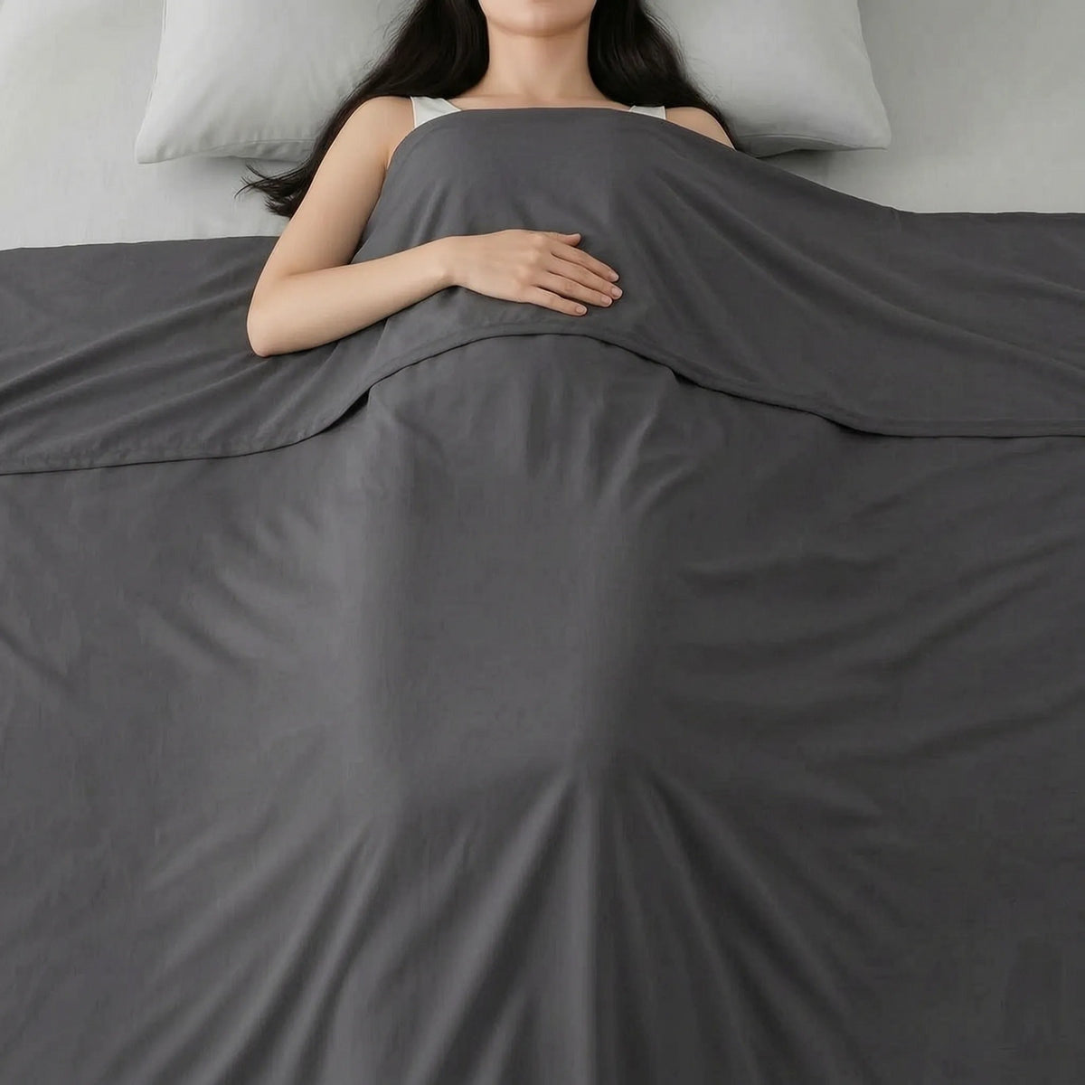 Thin smooth summer blanket over a sleeping woman in bed - dark grey