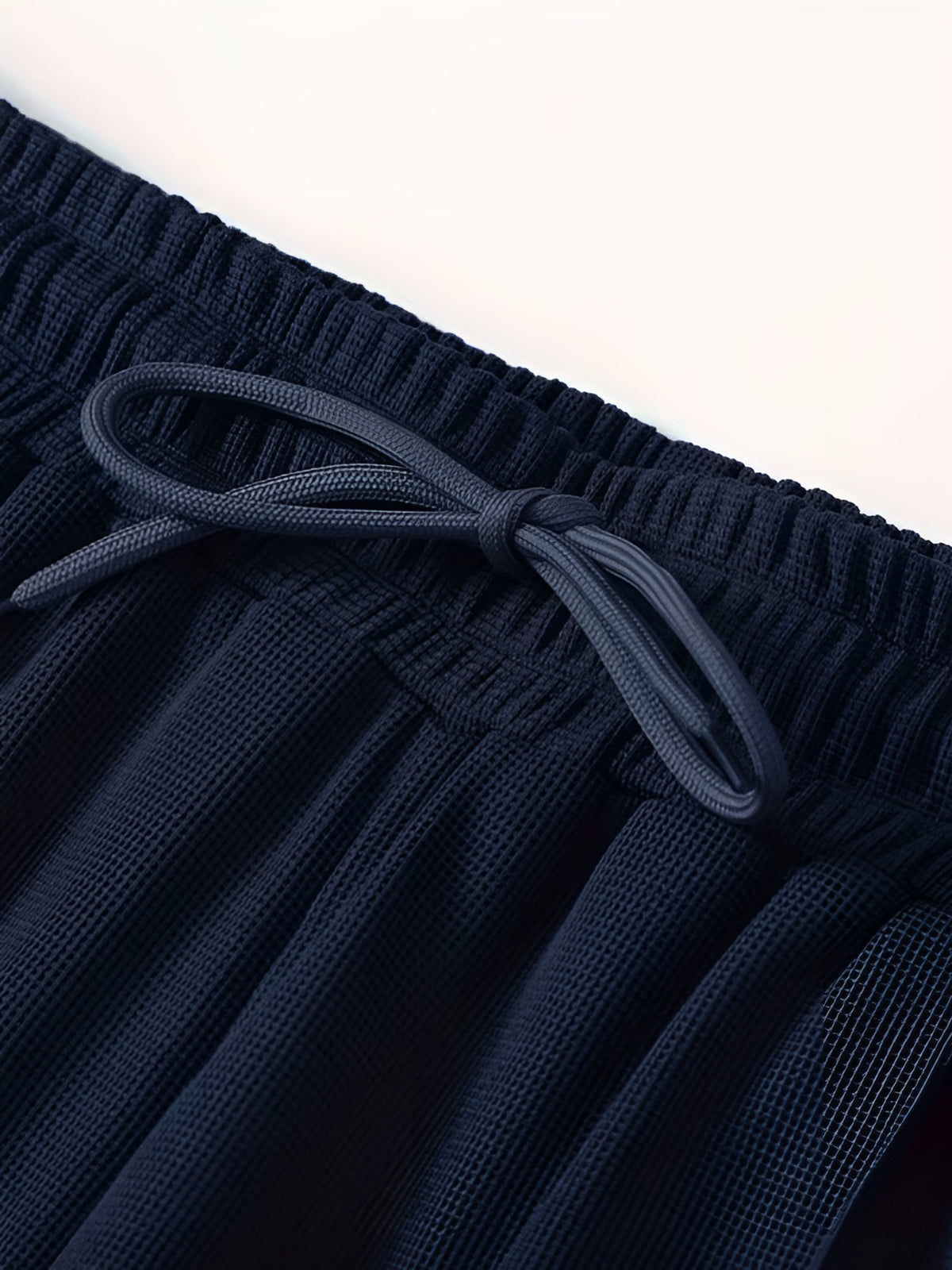 Close-up of the elastic drawstring waist on the navy tracksuit trousers