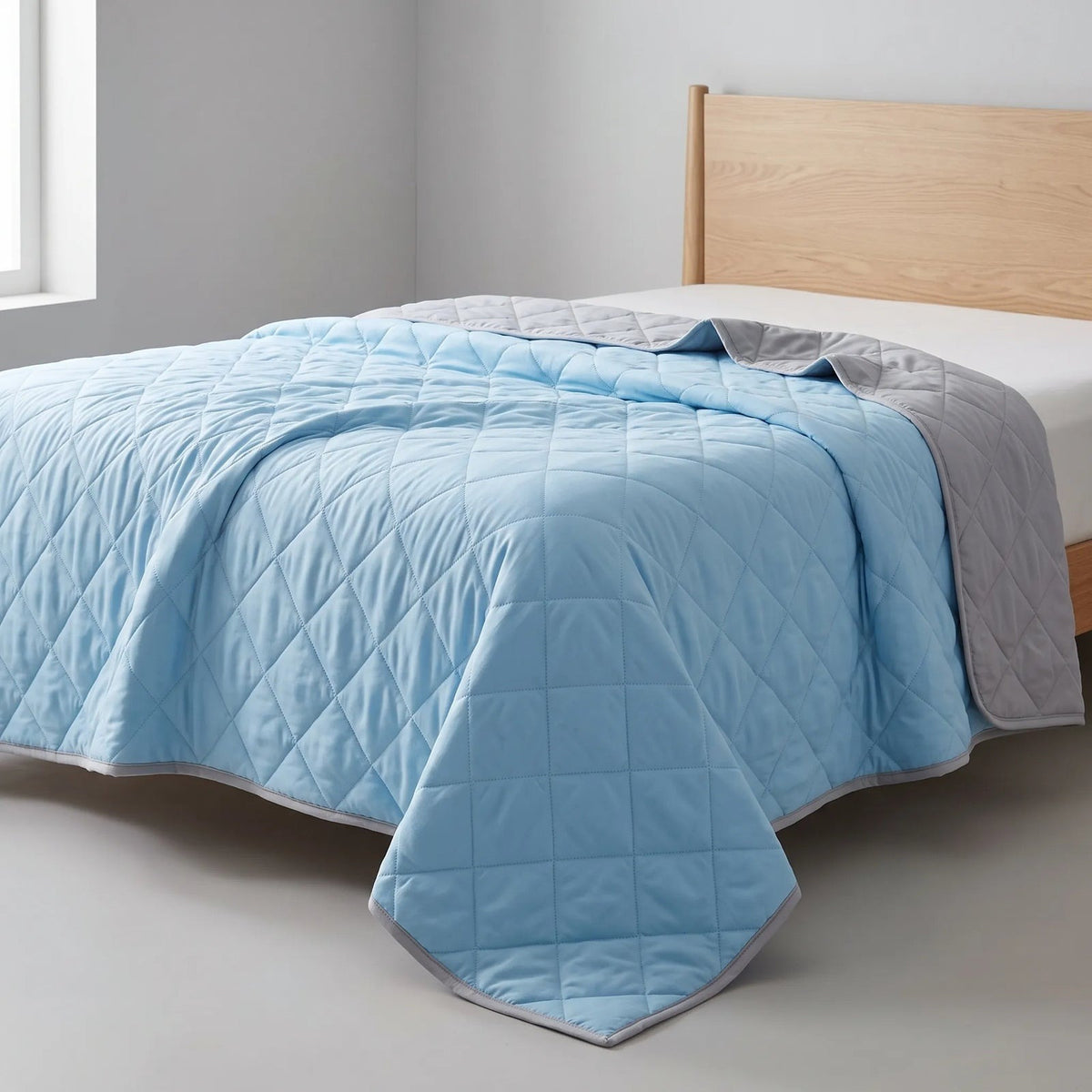 Quilted cooling blanket with diamond stitching and a grey underside on a bed