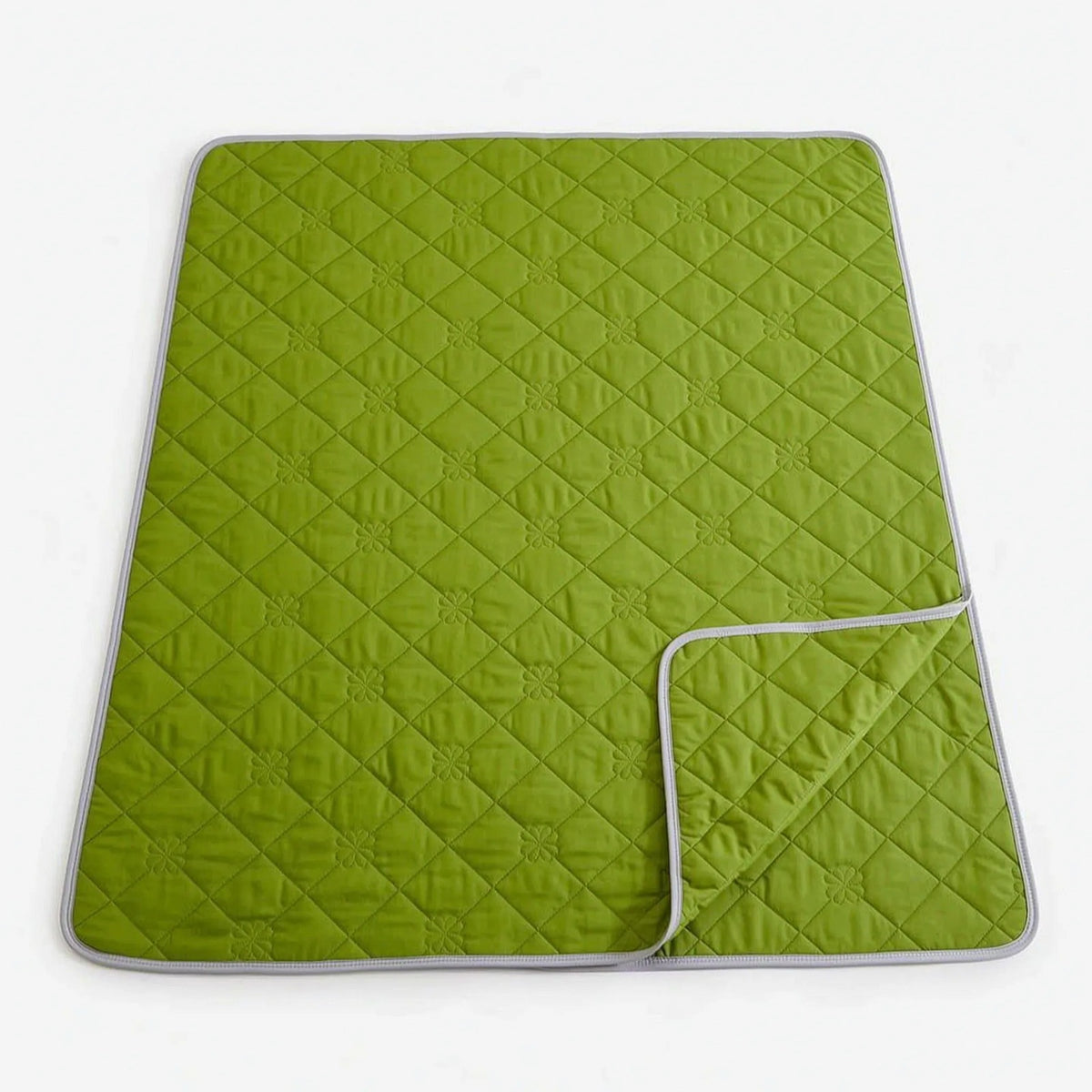 Quilted cooling blanket with diamond stitching and a grey underside on a bed - lime green