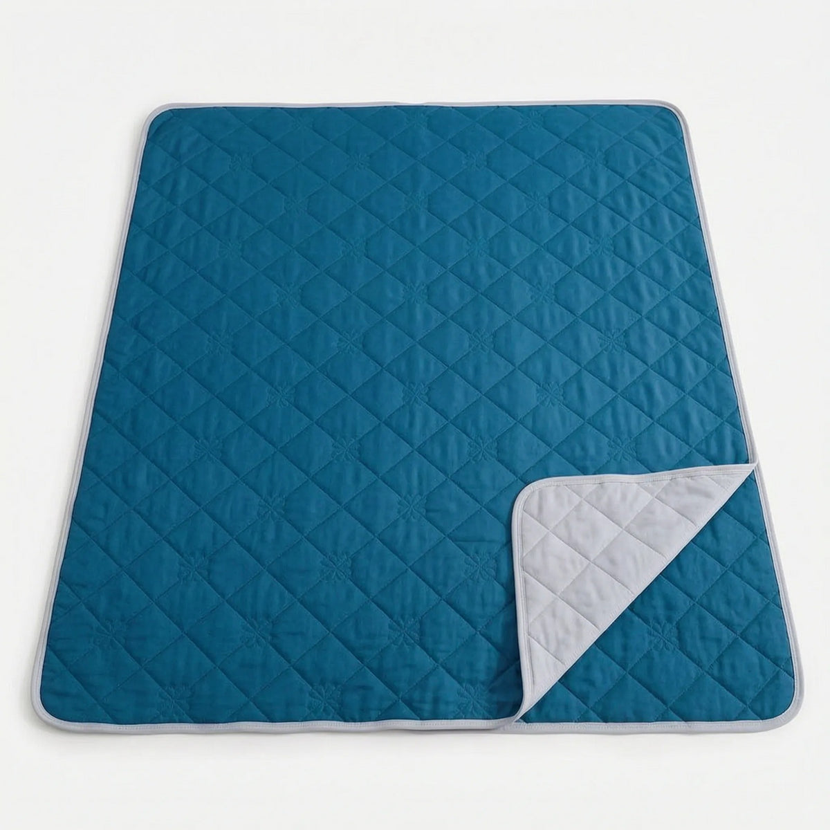 Quilted cooling blanket with diamond stitching and a grey underside on a bed - petrol blue
