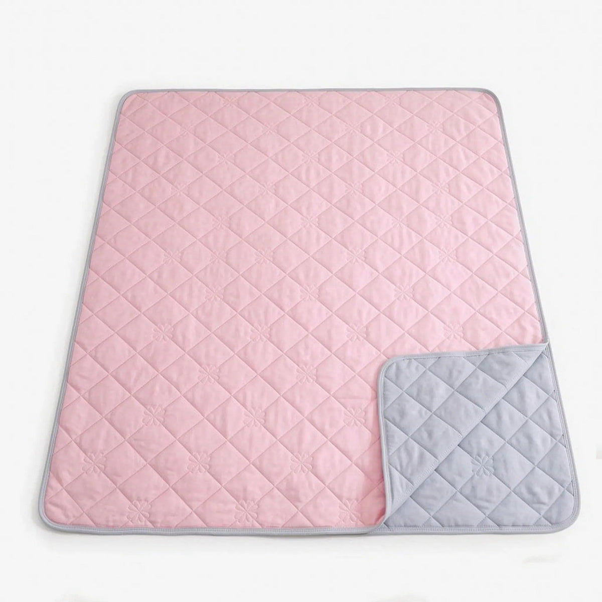 Quilted cooling blanket with diamond stitching and a grey underside on a bed - light pink
