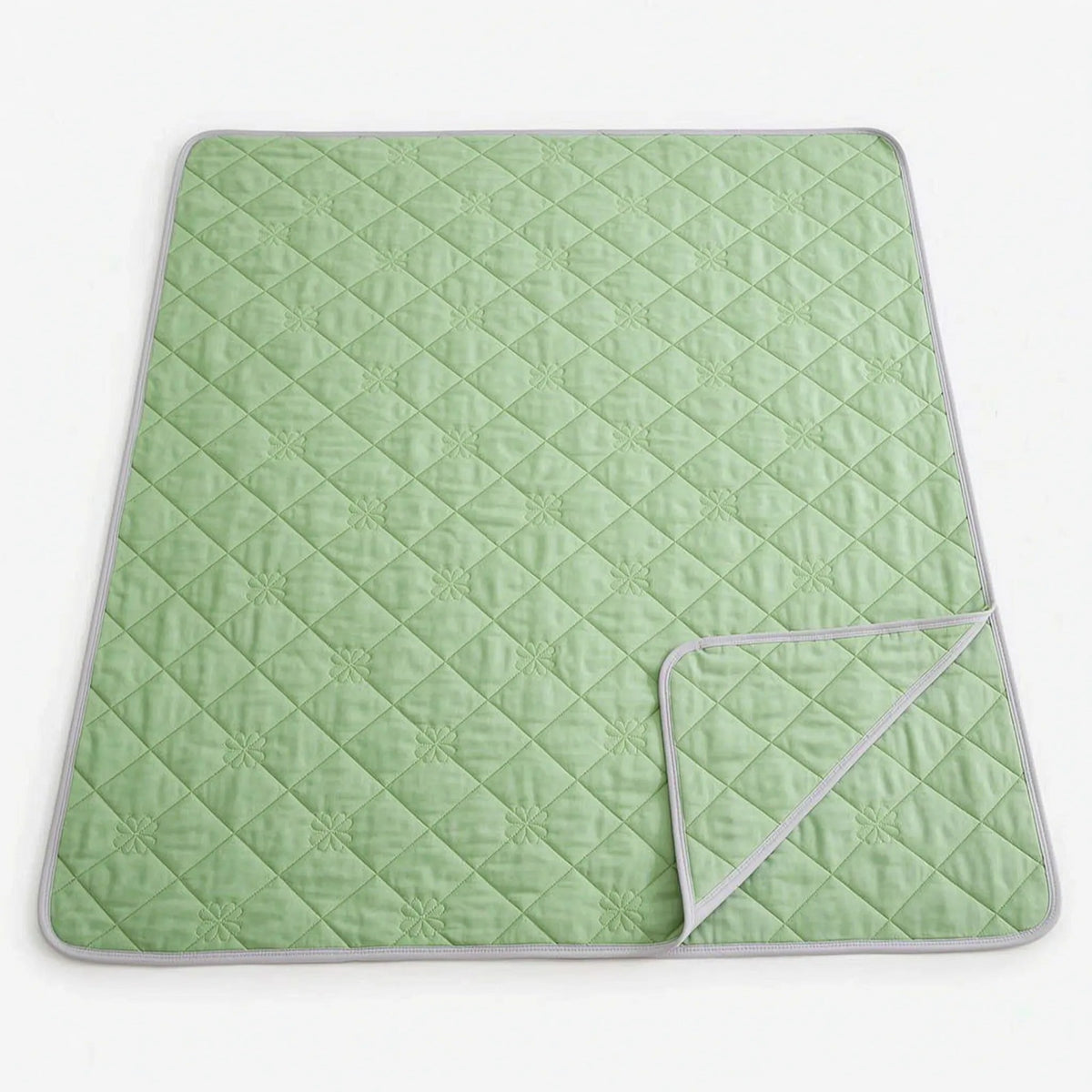 Quilted cooling blanket with diamond stitching and a grey underside on a bed - light green