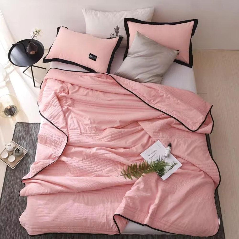 Thin quilted summer blanket with piping on a made bed - pink