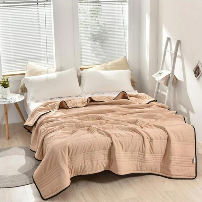 Thin quilted summer blanket with piping on a made bed - beige