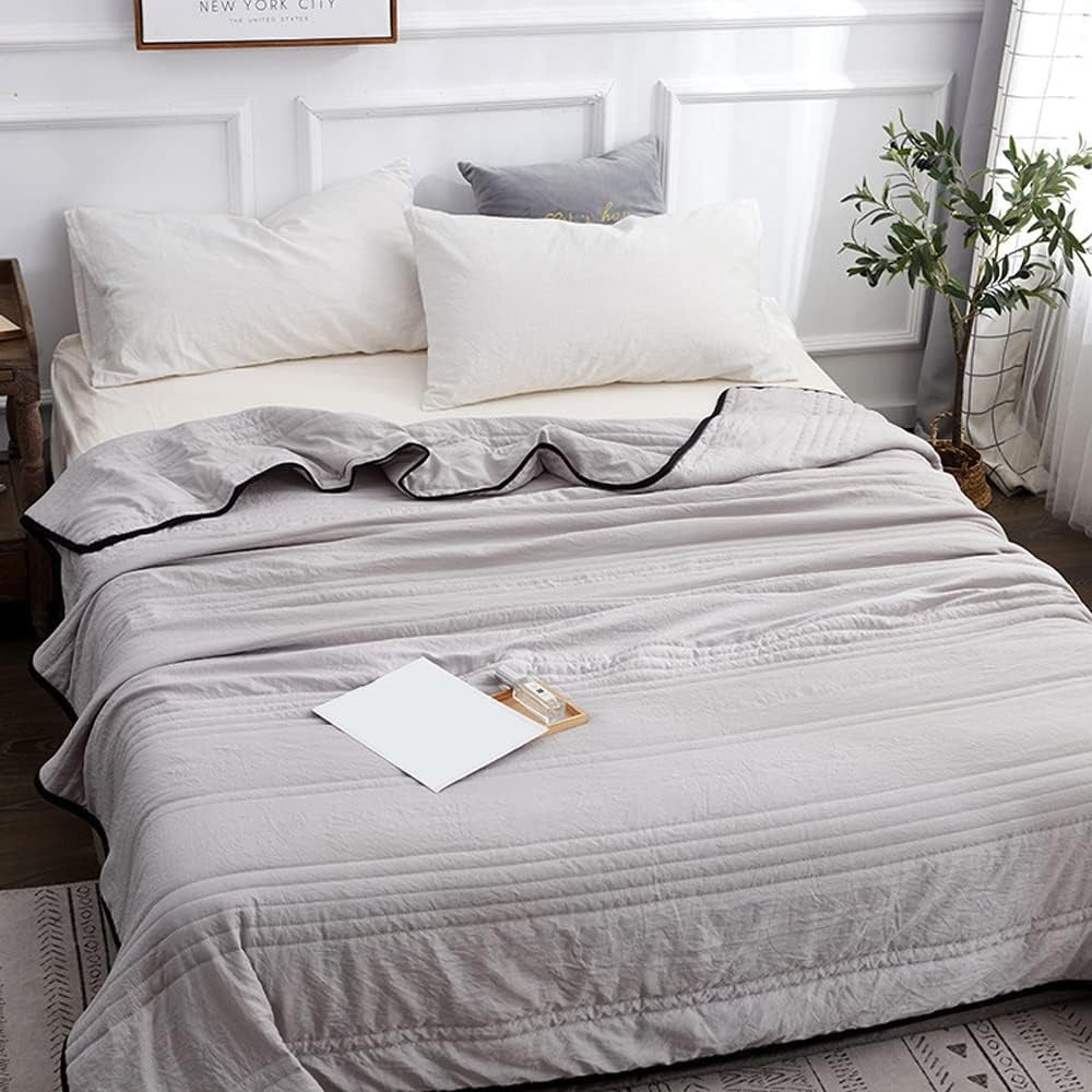 Thin quilted summer blanket with piping on a made bed - grey