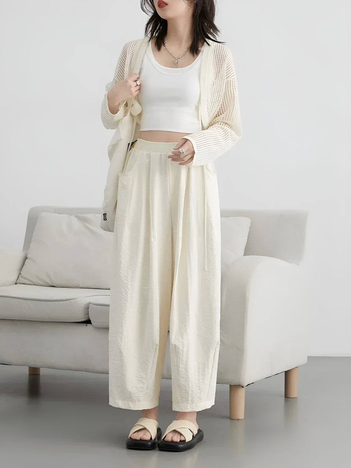 Women's cream wide-leg trousers with pleats, standing by a sofa