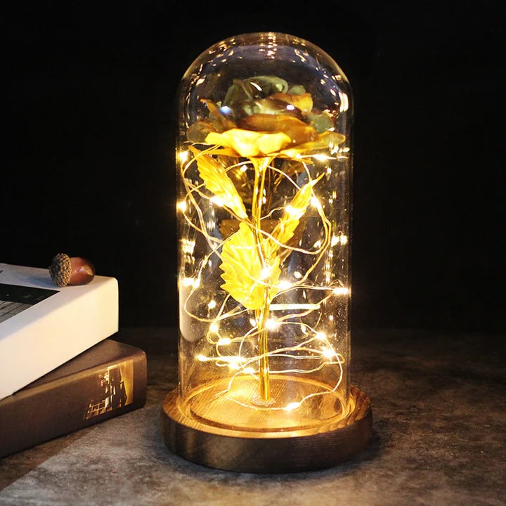 Artificial rose under a clear dome with LED string lights around the stem, on a round wooden base - gold