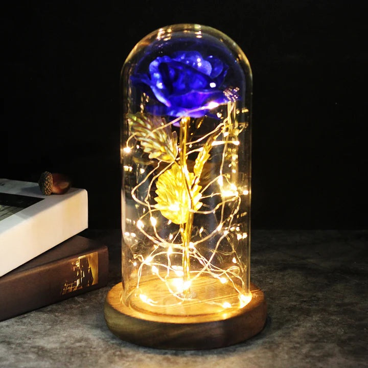 Artificial rose under a clear dome with LED string lights around the stem, on a round wooden base - blue