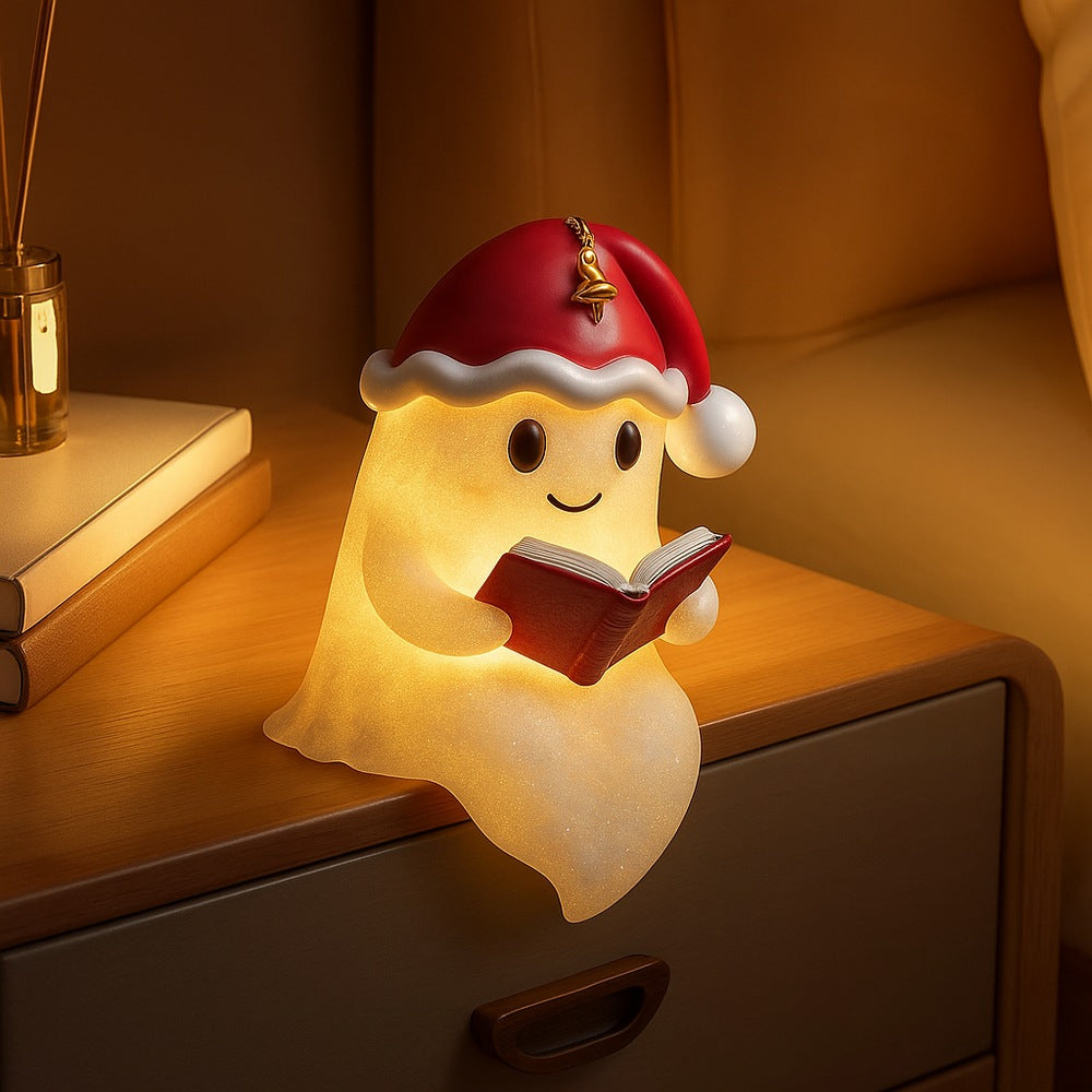 White ghost lamp in a red Santa hat with a bell, holding a red book and glowing warm yellow