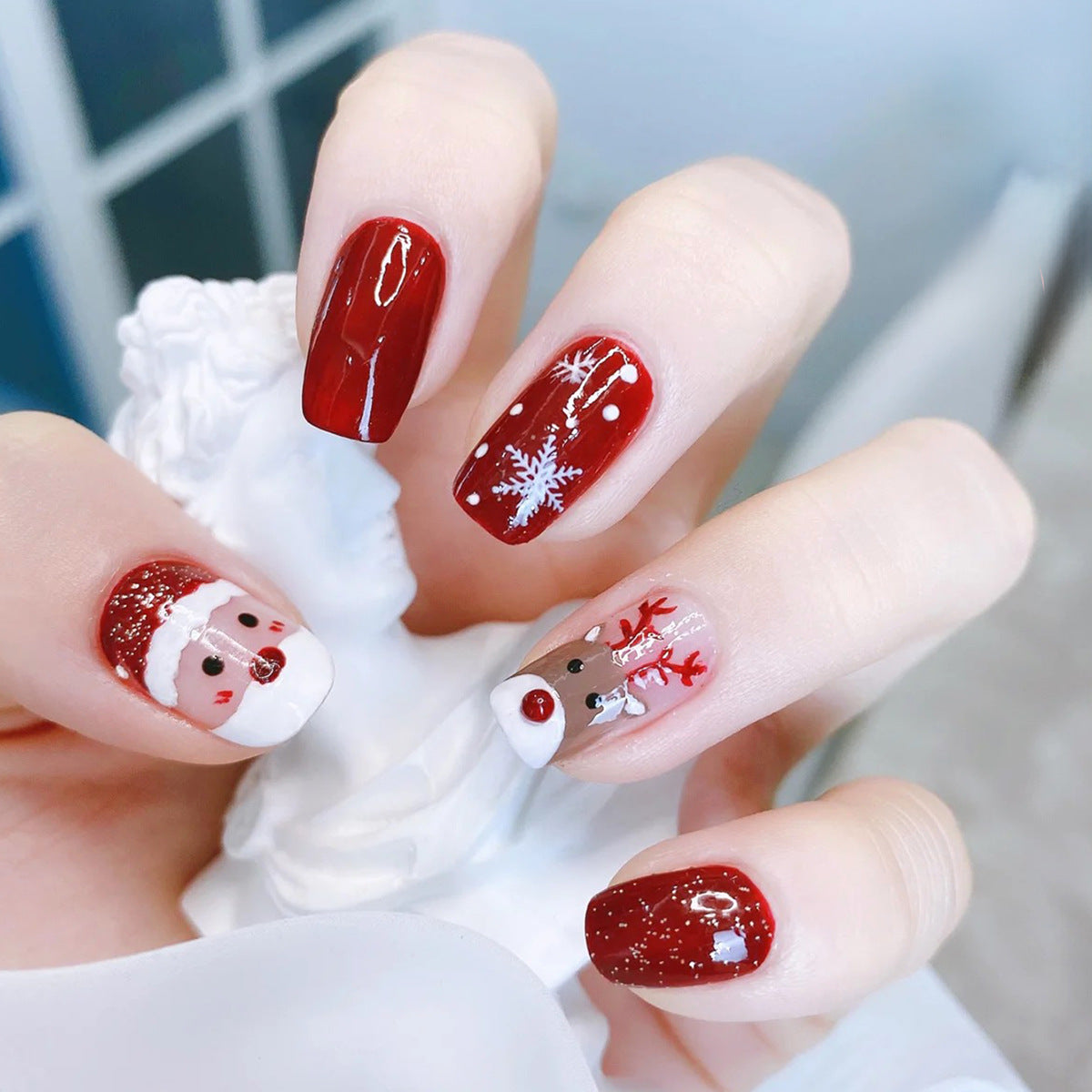 Christmas press-on nails with a festive print, applied on a hand - red with father christmas and reindeer