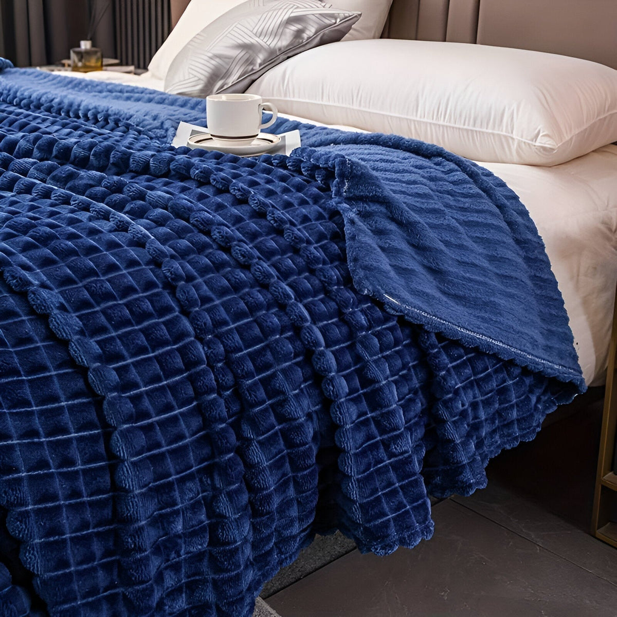 Coral fleece blanket with a square grid texture over a bed - royal blue