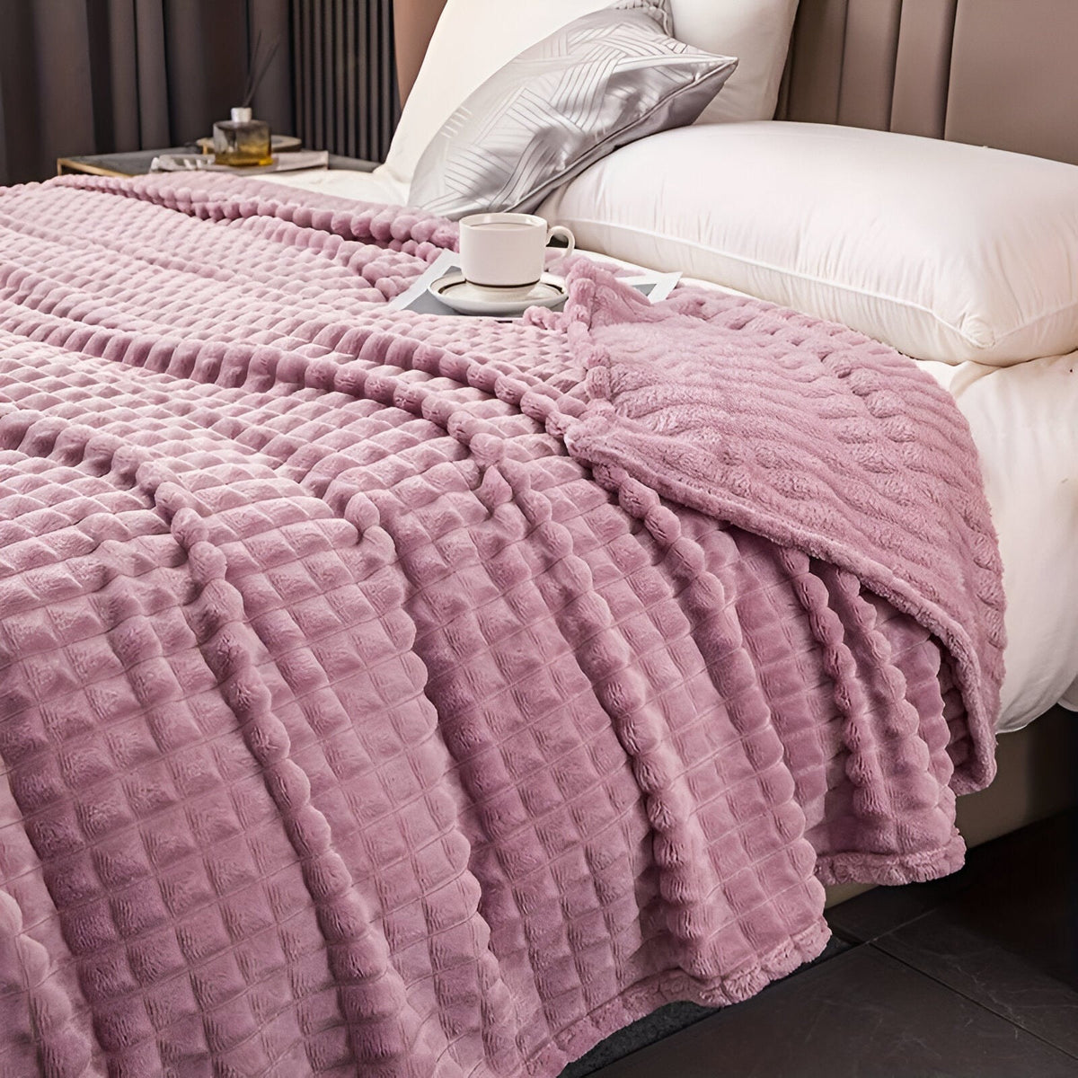 Coral fleece blanket with a square grid texture over a bed - mauve