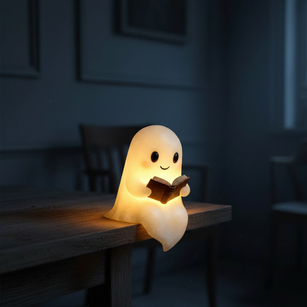 White ghost lamp with black eyes and pink cheeks holding an open brown book, glowing warm yellow