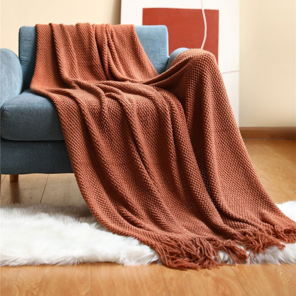 Knitted throw with a bobble texture and tassels over a sofa - rust