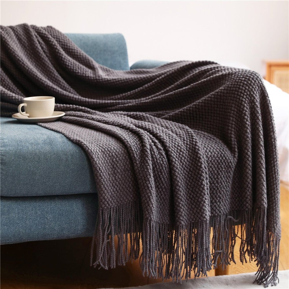 Knitted throw with a bobble texture and tassels over a sofa - dark grey