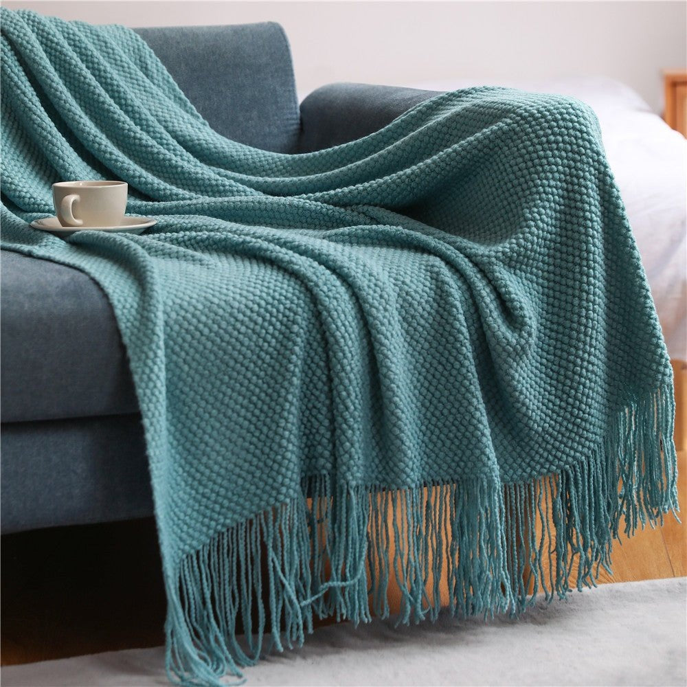 Knitted throw with a bobble texture and tassels over a sofa - teal
