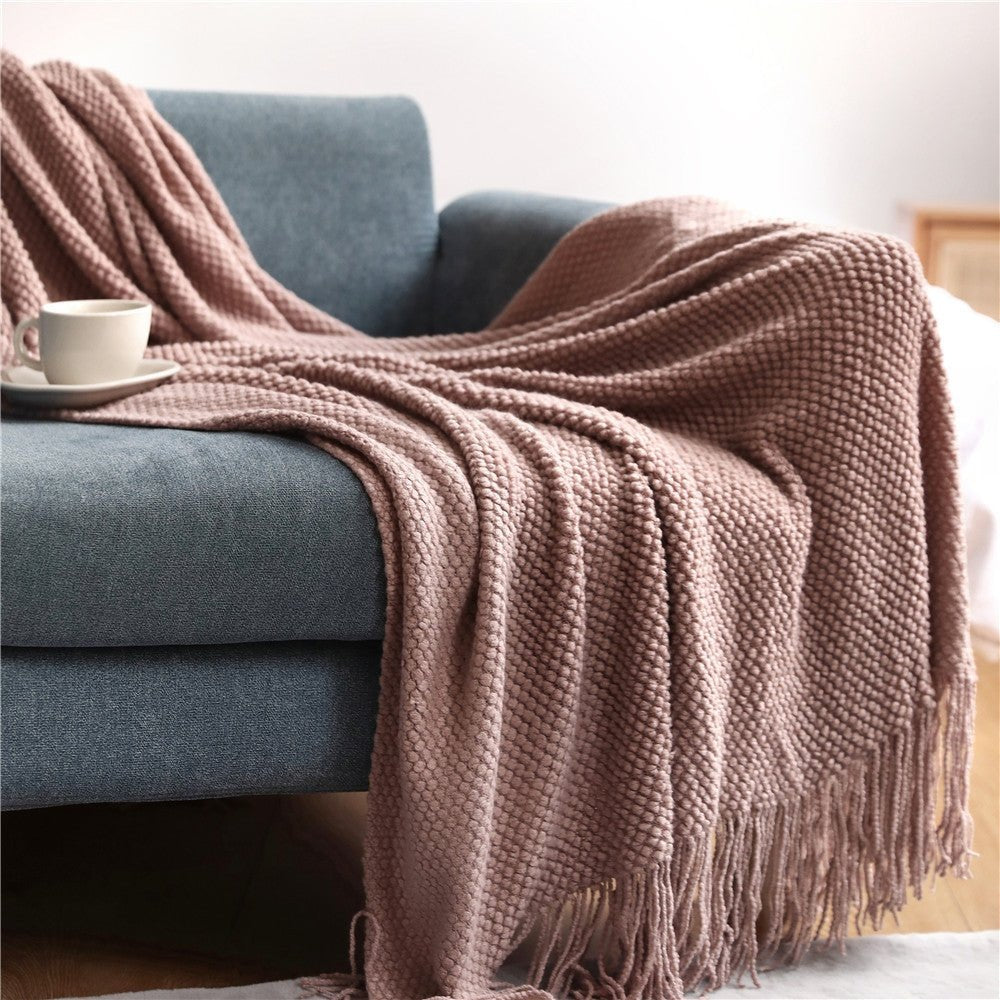 Knitted throw with a bobble texture and tassels over a sofa - dusty pink