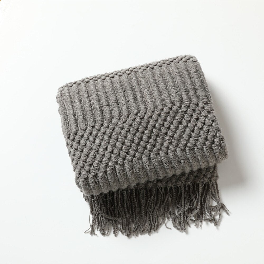 Knitted throw with a Scandinavian pattern and tassels over a chair - grey