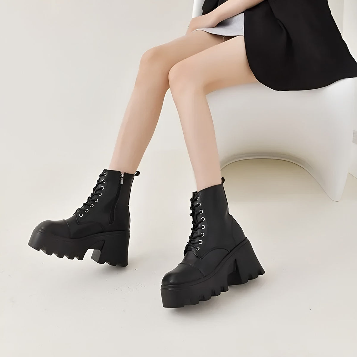 Black platform ankle boots with a block heel, worn seated with a black skirt