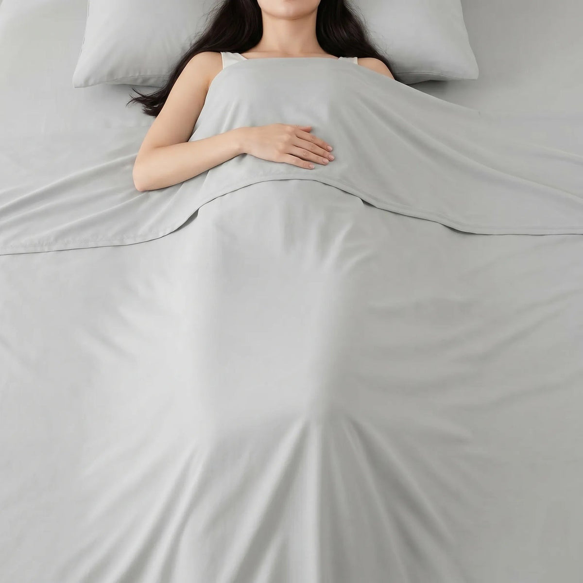 Thin smooth summer blanket over a sleeping woman in bed - light grey