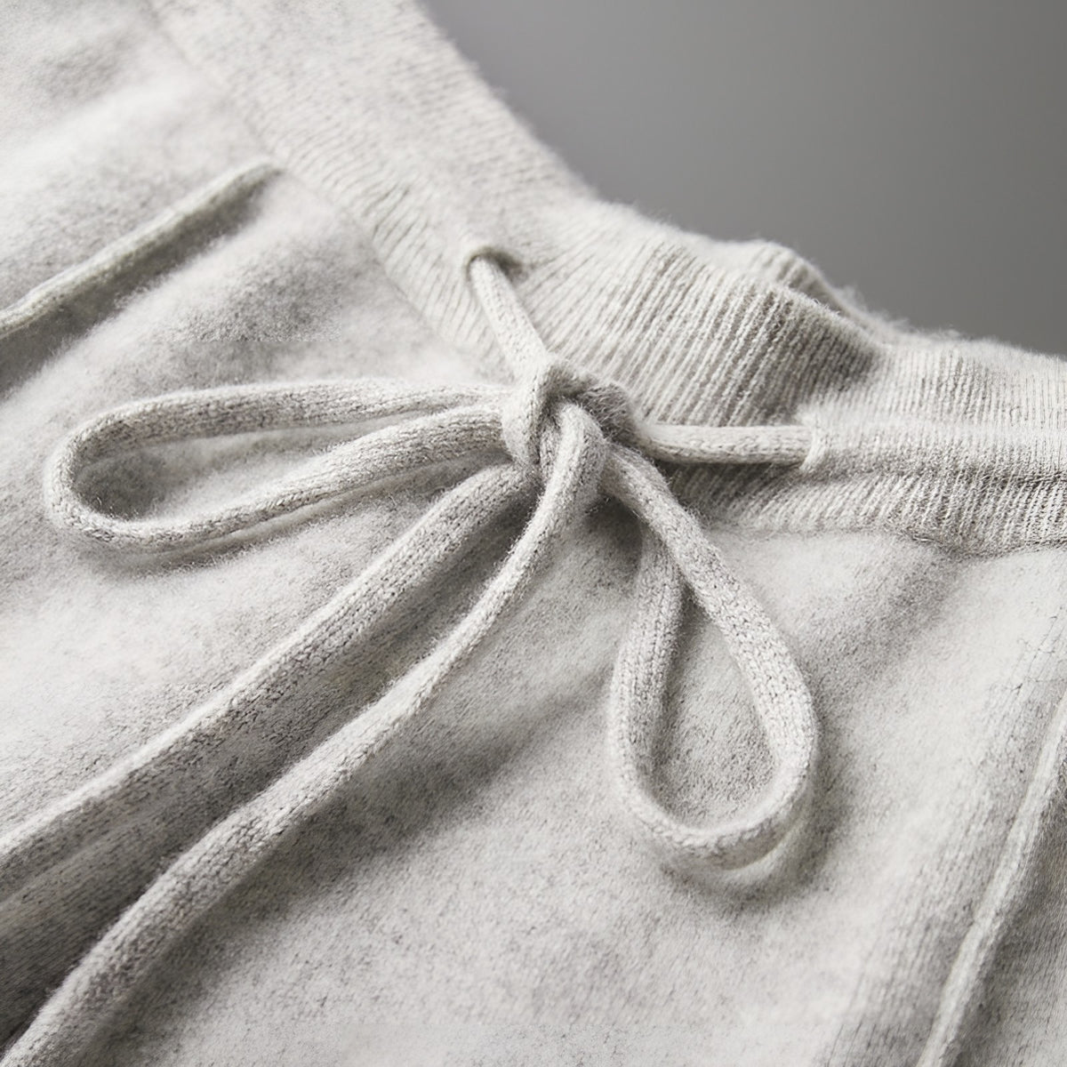 Close-up of the ribbed waistband and drawstring on the light grey knitted trousers