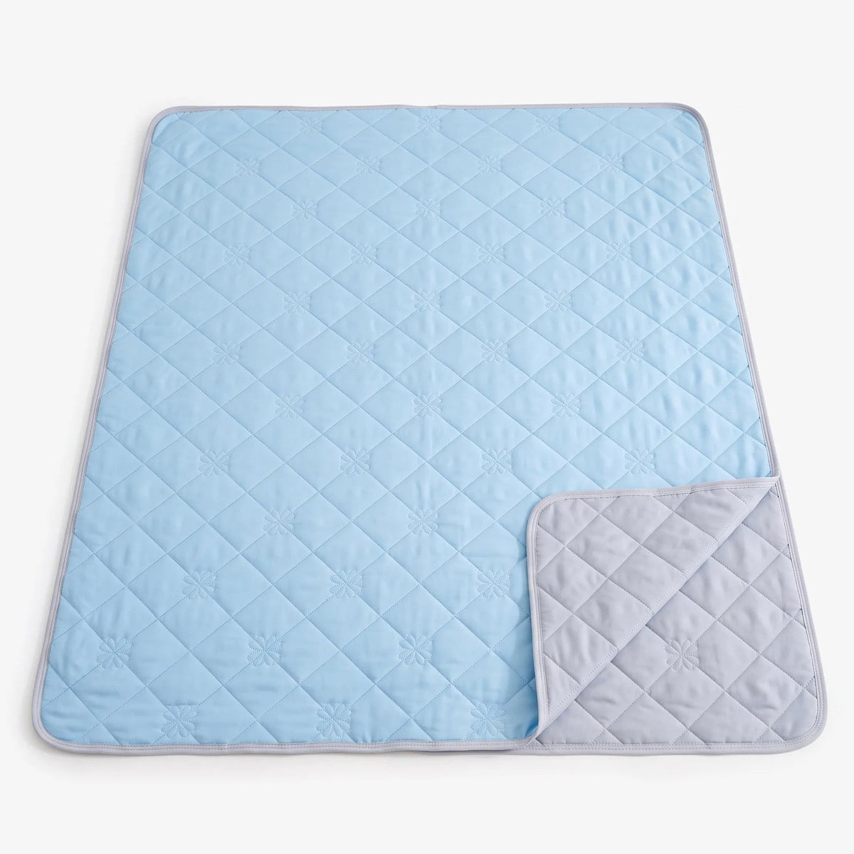 Quilted cooling blanket with diamond stitching and a grey underside on a bed - light blue