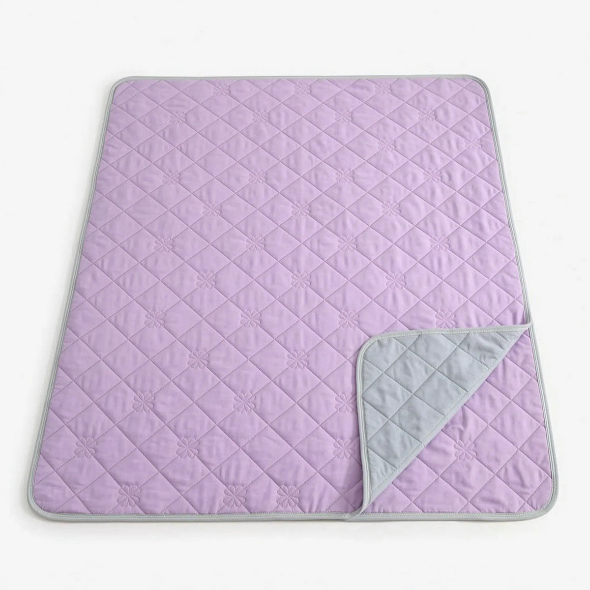 Quilted cooling blanket with diamond stitching and a grey underside on a bed - lilac