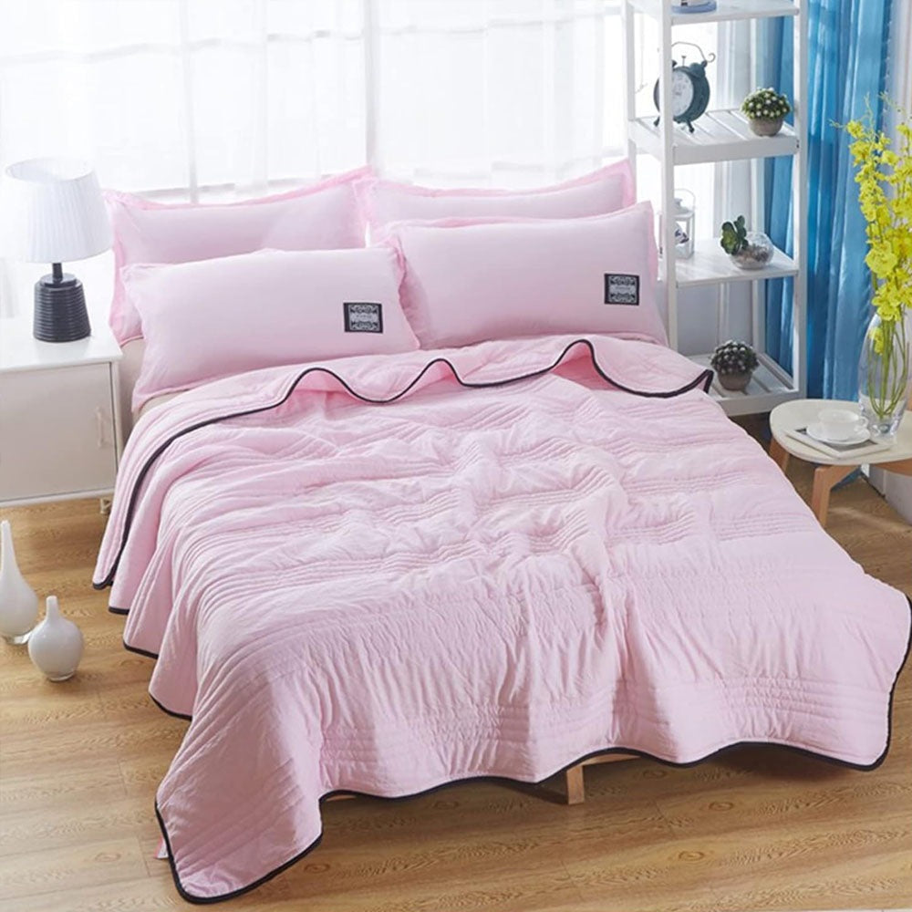 Thin quilted summer blanket with piping on a made bed - light pink